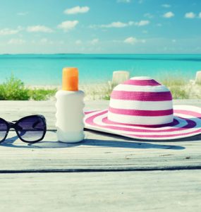 Sun hat, sun glasses and sun lotion on a table overlooking a beach