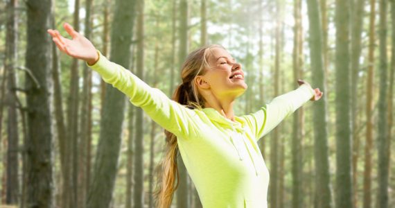 Happy woman in the woods with arms stretched out