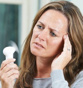 Woman using a hand held fan to cool a hot flush