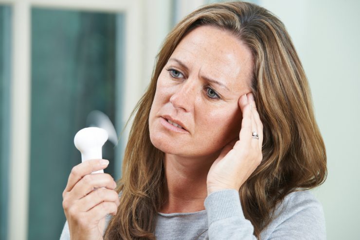 Woman using a hand held fan to cool a hot flush