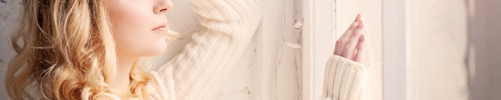 Close up of woman looking lout of a window whilst feeling sad