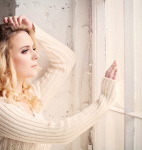 Close up of woman looking lout of a window whilst feeling sad