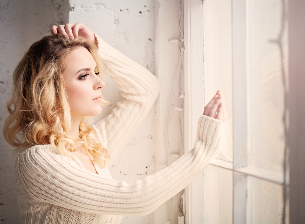 Close up of woman looking lout of a window whilst feeling sad