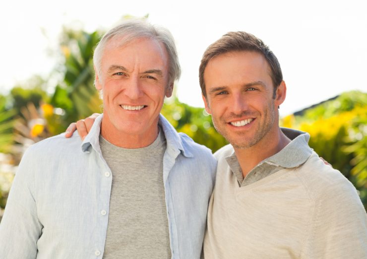 A middle-aged man and grown up son smiling
