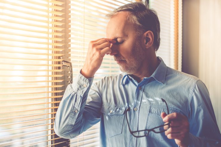 CLose up of a man holding his head to represent being tired and headachy