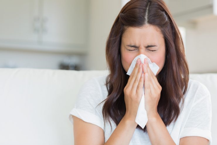 Close up of woman with a cold blowing her nose with a tissue.