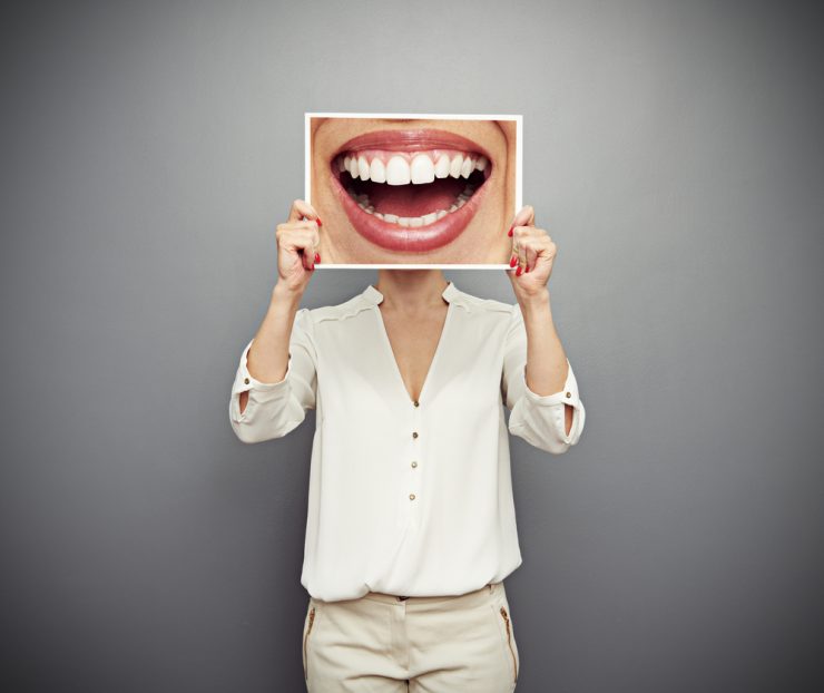 Woman holding an oversized photo of a smiling mouth over her face