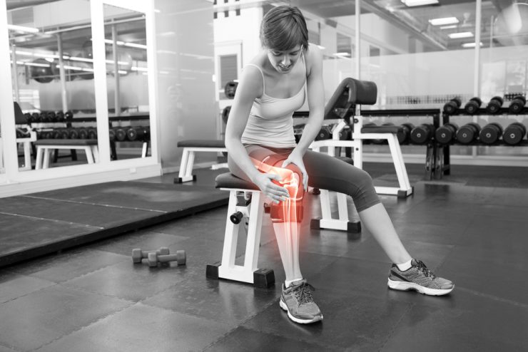 Woman at the gym sitting on a bench with joint pain indicated by a red glow around her knee