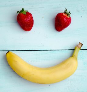 two strawberries and a banana made to look like a happy face on a blue wooden background