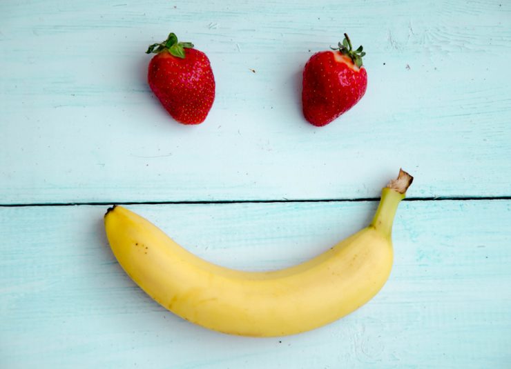 two strawberries and a banana made to look like a happy face on a blue wooden background