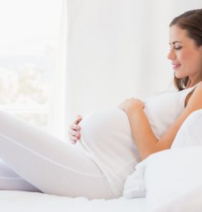Pregnancy shown by image of pregnant woman lying on bed smiling and cradling her stomach