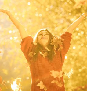 Woman in autumn arms outstretched enjoying the autumn leaves falling