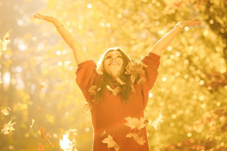 Woman in autumn arms outstretched enjoying the autumn leaves falling