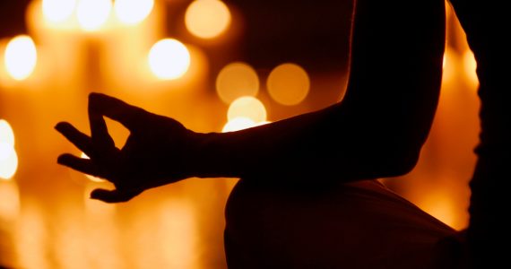 Woman in shadow meditating by candlelight to represent calm