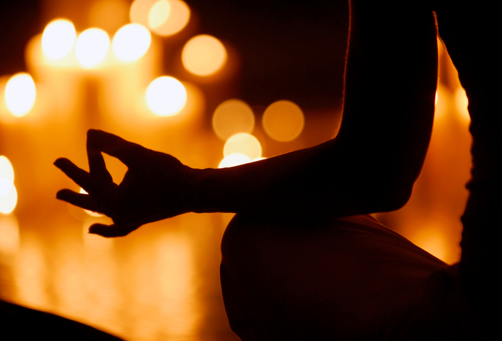 Woman in shadow meditating by candlelight to represent calm