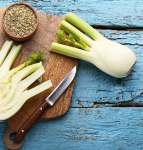 Whole fennel cut in half and fennel seeds on a wooden board