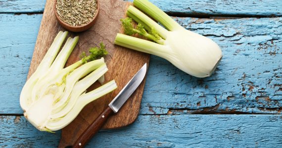 Whole fennel cut in half and fennel seeds on a wooden board