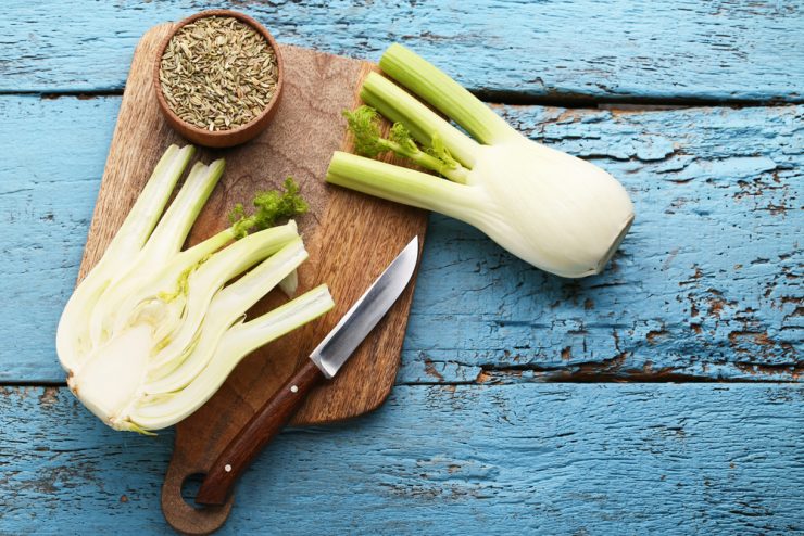 Whole fennel cut in half and fennel seeds on a wooden board