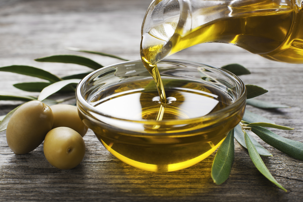 A bottle pouring olive oil into a bowl surrounded by olives